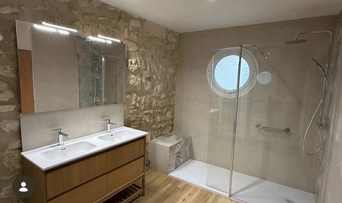 Salle de bain après rénovation : douche vitrée, vanité double en bois et pierre naturelle
